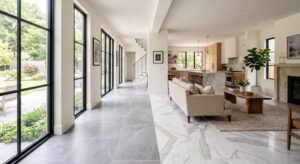 A brightly lit, modern open concept home interior showcasing a transition between elegant ceramic floor tiles and luxurious natural stone flooring.